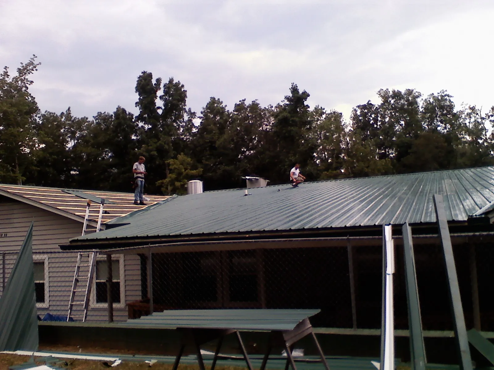 Two roofers installing green metal panels above a covered porch in Columbus